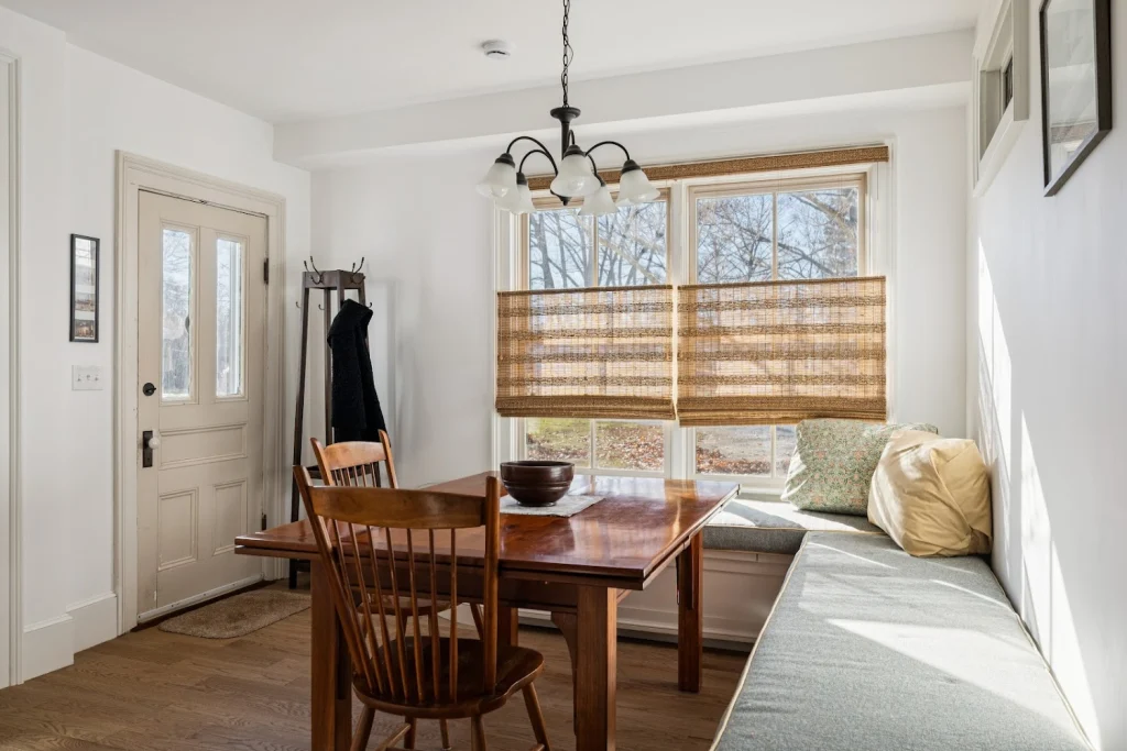 Cozy dining nook with a wooden table, chairs, long window seat, and light-filtering blinds