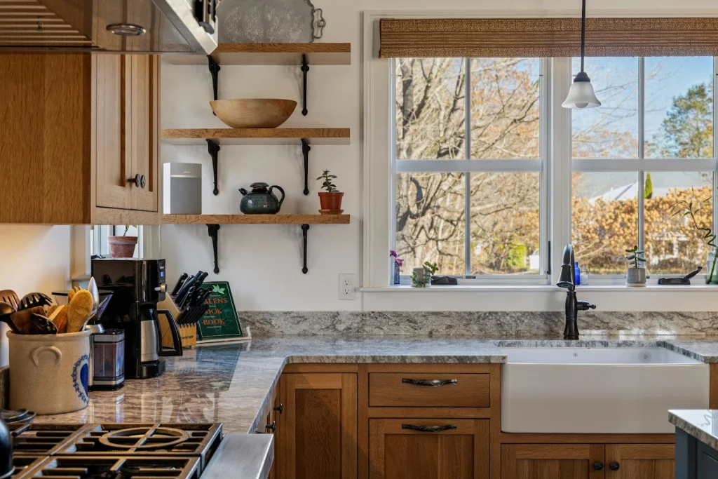 Modern kitchen with wood cabinets, granite counters, open shelves, white farmhouse sink, and large window