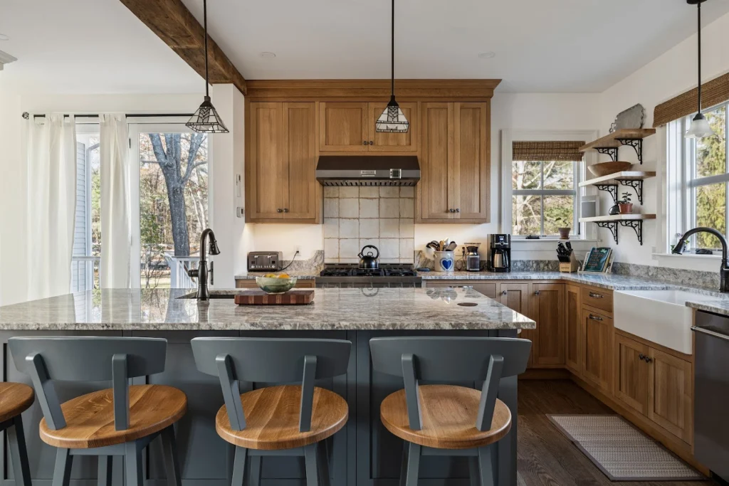 Modern rustic kitchen with wood cabinets, granite island, dark blue bar stools, and outdoor view