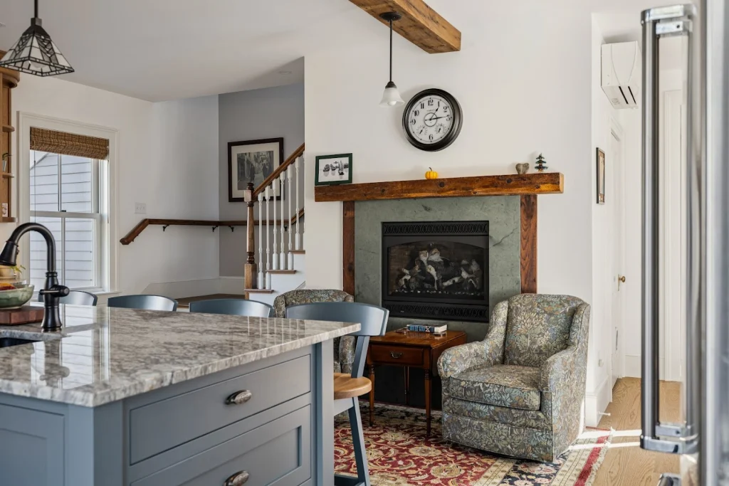 Cozy living room and kitchen with fireplace, armchairs, kitchen island, and staircase