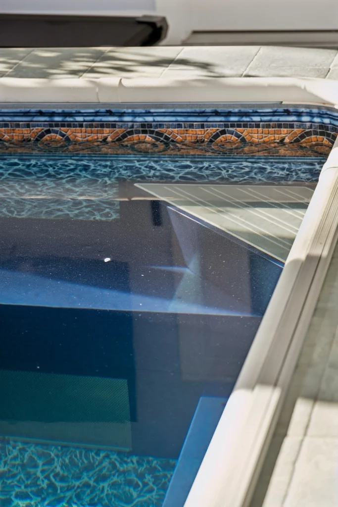 Overhead view of a pool with decorative tiles, blue water, and a partially deployed white pool cover