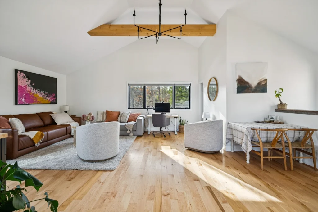 Spacious open-concept living room with light wood floors, a brown leather sofa, and a home office desk