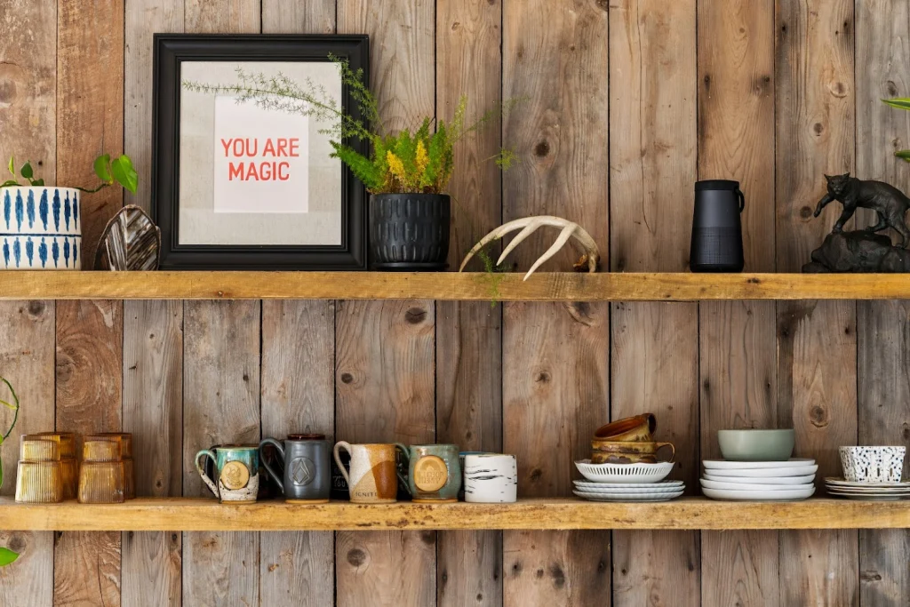 Rustic wooden wall shelves displaying plants, decor, mugs, plates, and a Bluetooth speaker
