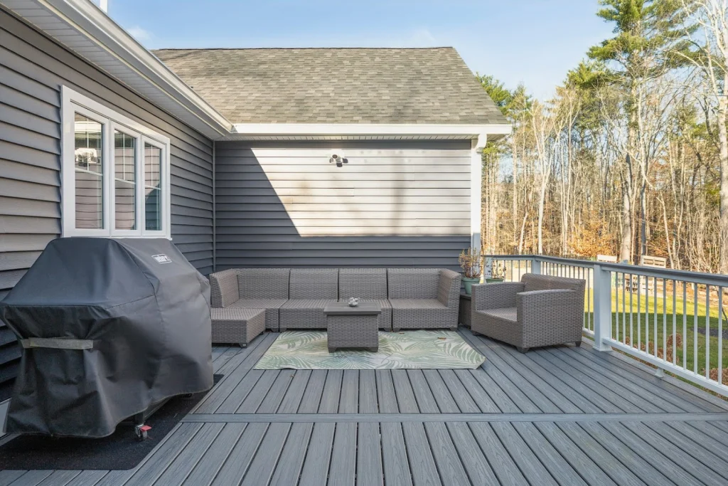 Gray composite deck with outdoor furniture, barbecue grill, and view of bare trees