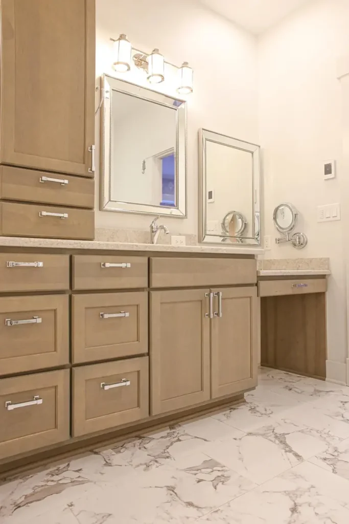 Bathroom vanity with tall linen cabinet, stained wood drawers, chrome pulls, framed mirrors, and marble-look tile