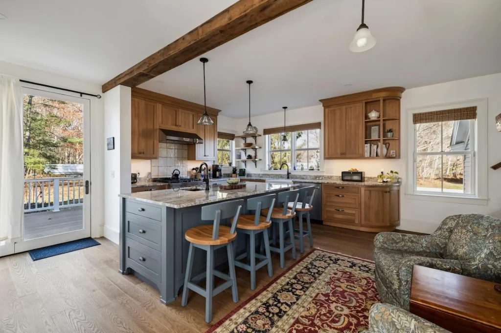 Open kitchen with wood cabinets, gray island with swivel barstools, granite counters, and wood beam